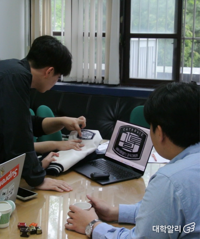 가대알리 조우진 편집국장, 권민제 대표(왼쪽)가 김민구 총학생회장(오른쪽)과 함께 직접 준비한 21학번 학잠과 샘플 사진 속 로고를 비교하고 있다. (사진=<strong>김단비 기자</strong>) 